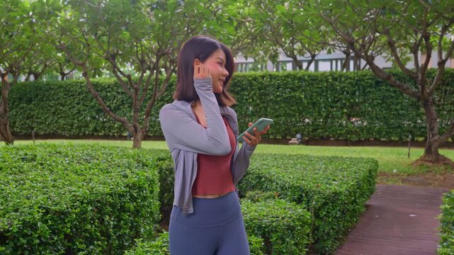 Asian sporty woman wear earphone using smartphone standing in park.