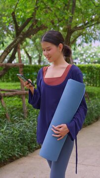 Asian sport woman holding yoga mat and using smartphone in park