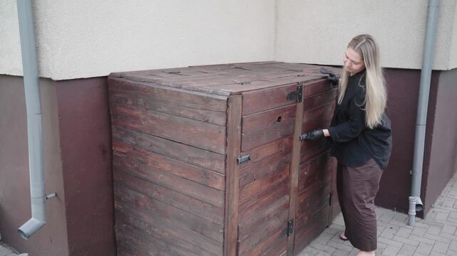 Black-gloved DIYer fights with a warped wooden bin enclosure door that will not close, suggesting poor construction and needed repair.