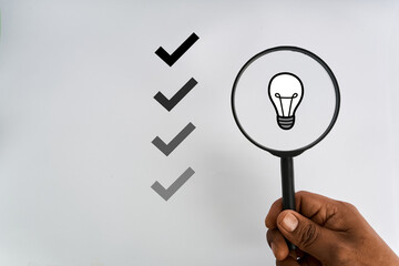 Hand holding a magnifying glass over a light bulb beside check marks representing idea validation  © kaliel