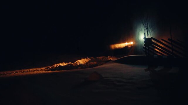 A Tractor Drives Through Deep Snow At Night With Its Headlights Illuminating The Winter Landscape. Static Shot