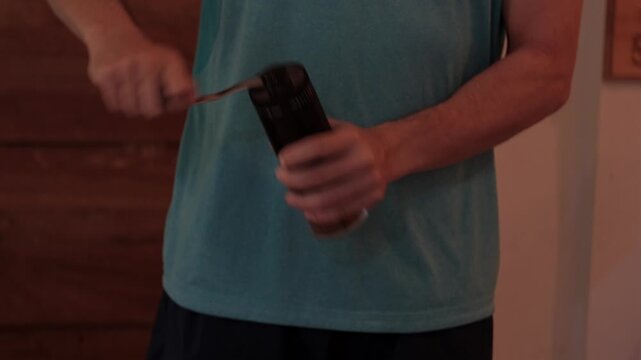 Medium shot of a young man grinding coffee indoors with a handheld manual grinder, showing a simple home brewing preparation process