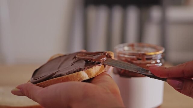 Slow motion captures woman spreading hazelnut chocolate cream onto white bread