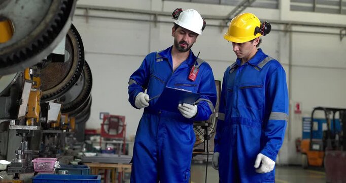 Senior worker mentoring young technician while inspecting parts at press machine in factory