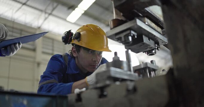 Senior worker mentoring young technician while inspecting parts at press machine in factory