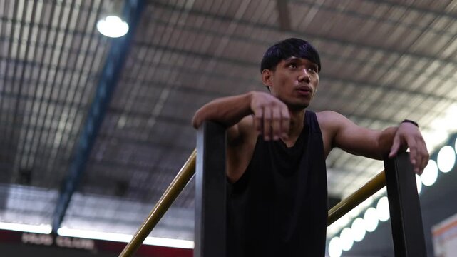 Tired athlete resting after an intense workout. Fit Asian man in black sportswear resting on parallel bars. Exhausted but happy athlete recovering after an intense training session.