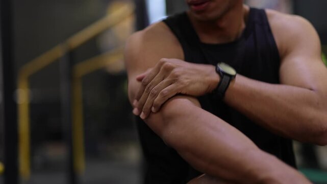 Athletic man massaging sore muscle after workout. Fit man feeling muscle ache and massaging his arm at the gym. Sportsman suffering from pain after intense training and workout.