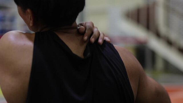 Athlete with shoulder pain massaging his sore muscle. Rear view of a man experiencing shoulder discomfort after a workout. He is massaging his tense and aching muscles to relieve the pain.