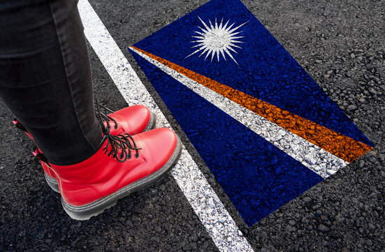 a woman with a boots standing on asphalt next to flag of Marshall Islands and border
