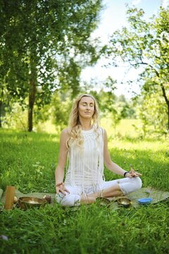 A woman peacefully meditates on a mat in a vibrant green park, surrounded by trees and nature