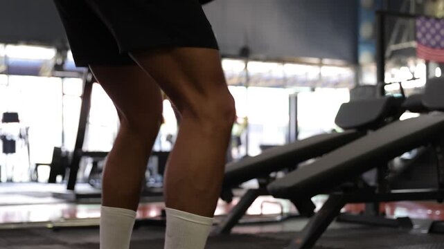 Muscular man performing squats in the gym. Low angle view of an athletic man with muscular legs doing squats. A bodybuilder exercising his lower body during a strength workout routine.