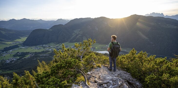 Hiker standing on hiking path between mountain pines, view of mountain landscape with Pillersee, descent from Heimkehrerkreuz, Nuaracher H&ouml;henweg, Loferer Steinberge, Tyrol, Austria