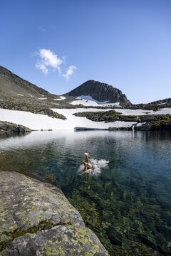 Young man jumps into a mountain lake, Sk&aring;lavatnet, ascent to the summit of Sk&aring;la, Norway