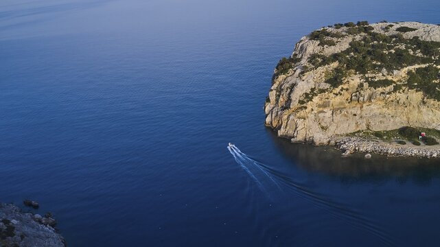 Drone shot, Small boat navigating through the clear blue water along a steep cliff, Anthony Quinn Bay, Vagies Bay, Rhodes, Dodecanese, Greek Islands, Greece