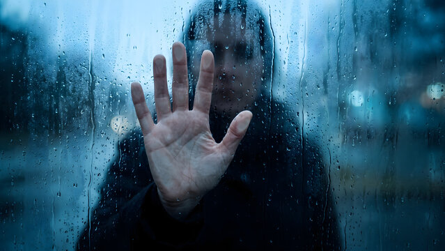 Sad Woman Pressing Hand Against A Rain Covered Windowpane Looking Out With A Gloomy Expression