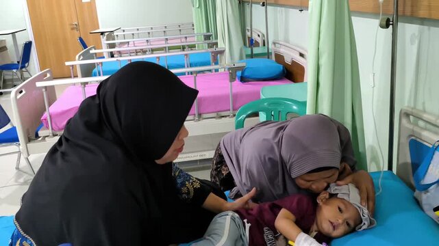 Caring mother wearing a hijab comforting her child in a hospital ward, showing love, support, and family bonding during medical treatment.