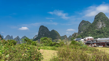 Obraz premium Picturesque mountain landscape. High hills with rounded peaks and green vegetation on the slopes. In the foreground there is a meadow, grass, bushes. China. Yangshuo. 
