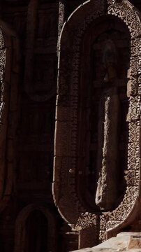 The stone carving shows a figure surrounded by intricate designs. This ancient work is found in a temple setting. The area appears remote with historical significance and culture.