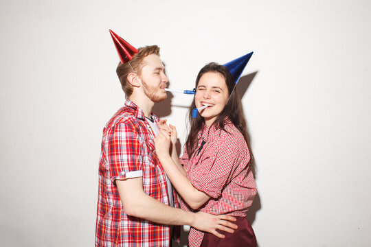 Happy young couple wearing party hats and celebrating together against a neutral background. Birthday, friendship and festive event concept.