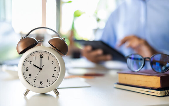 close up alarm clock 10 AM with blurred background asian businessman using computer working and start new online business, e-commerce