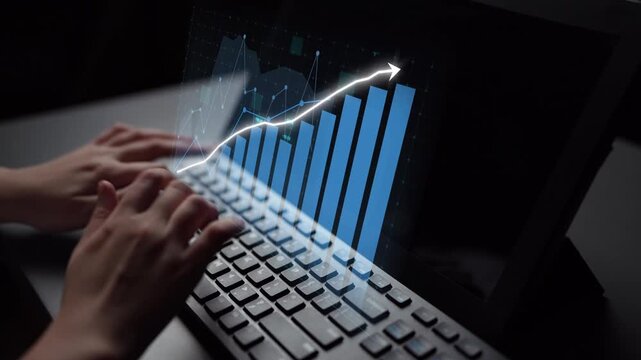 Close-up of hands typing on a laptop keyboard, with a bright data trend line graphic emerging from the screen, symbolizing growth and analysis in a tech-focused workspace. Copula