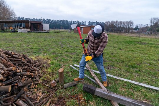 Full length shot of a man preparing firewood with a red axe outdoors on a cloudy day