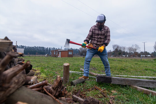 Worker in a plaid shirt chopping wood for winter outside a countryside cabin, horizontal shot
