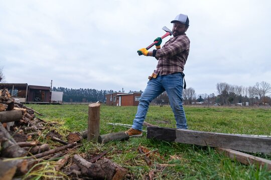 Mid-swing shot of a man lifting an axe to chop firewood in a rural field