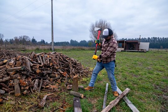 Active worker splitting timber with a hatchet outside a country cottage, horizontal shot