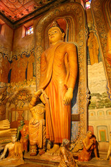 Obraz premium DIKWELLA, SRI LANKA - JULY 2026: Golden standing Buddha statue with ancient murals at Wewurukannala Raja Maha Viharaya shrine room.