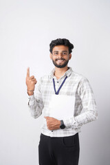 Fototapeta premium A smiling young man in a checkered shirt points upwards with his index finger against a plain white studio background.