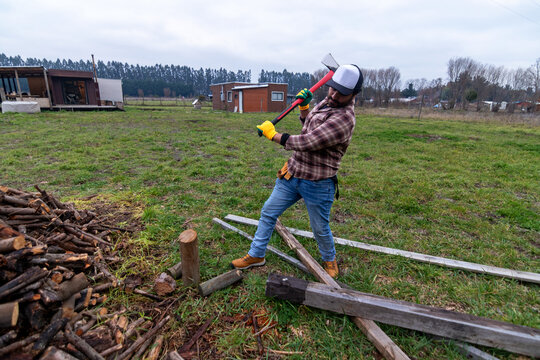 Man splitting logs with an axe on a grassy field in a rural setting