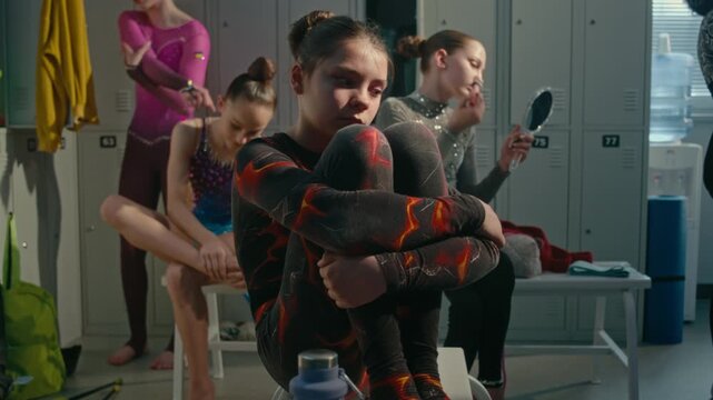 Young Athlete in Crowded Dressing Room, Holding Knees Tightly With Sad, Anxious Expression, While Teammates Busy Preparing For Tournament. Intense Psychological Pressure, Stage Fright in Youth Sports.