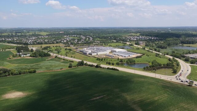 Aerial wide angle view of a modern data center facility surrounded by green fields and suburban roads 