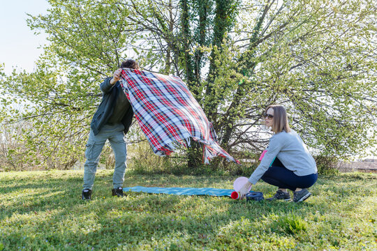 Friends Setting Up Picnic in Green Park on Sunny Spring Day