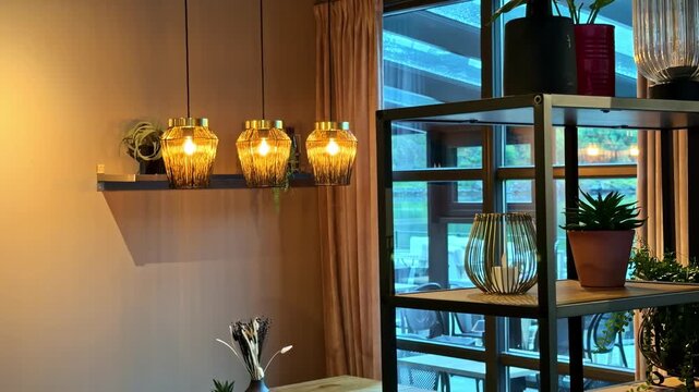 Warm pendant lights and indoor plants decorate a cozy modern cafe interior by a window
