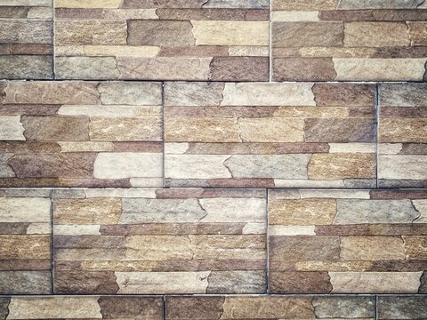 Close-up photograph of a decorative stone-look wall with layered rectangular tiles in beige, gray, and brown tones. Suitable as an architectural background, texture, or interior design concept.