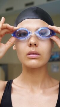 Young athletic woman in a swim cap looking at the camera and putting on her swimming goggles before a workout in the pool, demonstrating focus and preparation for a competitive race or training