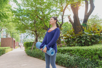 Fototapeta premium Asian Gen Z woman carrying yoga mat walking to park for wellness healthy lifestyle mindfulness and outdoor exercise.