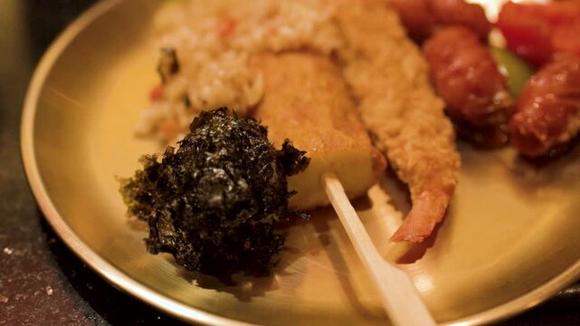 Close Up of Hand Picking Up Seaweed Rice Ball from Brass Plate