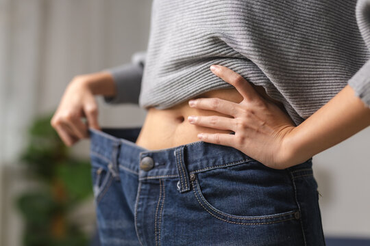 Close up confident slim woman wearing oversized old blue jeans showing successful weight loss diet results with flat bare stomach