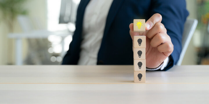 Building Innovation and Business Growth. Stacking wooden blocks with a glowing light bulb on top, representing innovation, business growth, strategic thinking, leadership and continuous improvement.