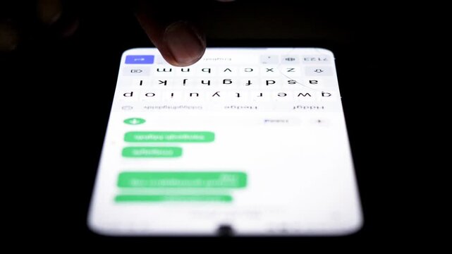 Night, hands typing repeated messages on a smartphone for spam messaging, anonymous communication, internet trolling, cyberbullying, and online harassment.