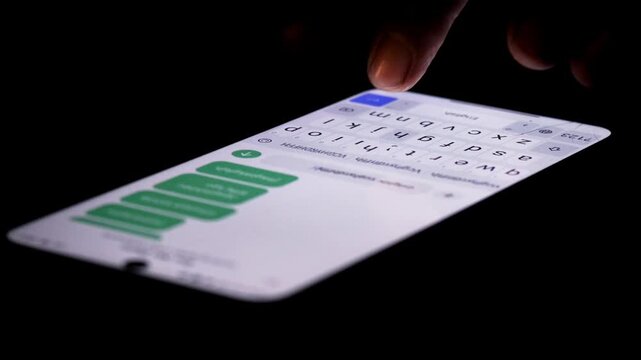 Night, hands typing repeated messages on a smartphone for spam messaging, anonymous communication, internet trolling, cyberbullying, and online harassment.