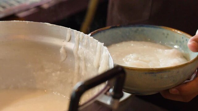 Chef Serving Hot Rice Congee Into Bowl From Metal Pot