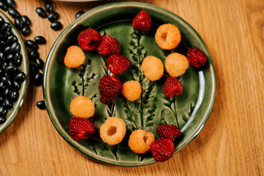Fresh red and golden raspberries on a rustic plate atop a wooden table
