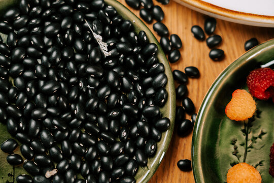 Black turtle beans piled high on a green ceramic plate with fresh raspberries nearby on a wood table