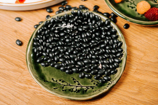 Black beans on a green plate on a wooden kitchen table in daylight