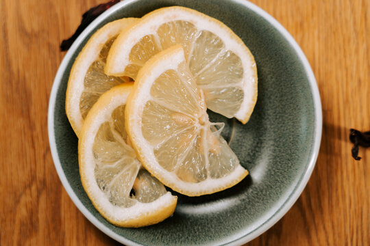 Freshly sliced yellow lemon segments arranged neatly inside a dark ceramic bowl on a wooden table