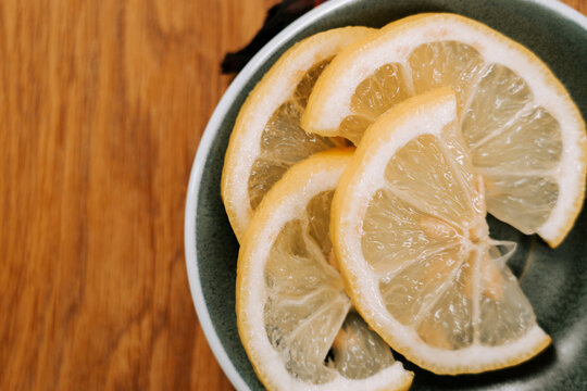 Fresh yellow lemon slices served in a green ceramic bowl on a wooden kitchen table during the day